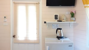 A room with a white door, a television mounted on the wall, a small shelf with a picture frame, a kettle, and a potted plant. - Hello Sunny Home (Pak Chong)