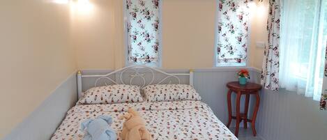 Un dormitorio con cama, cortinas florales, una mesita de noche con planta y un equipo de aire acondicionado.