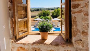 A stone-framed window with a view of a swimming pool and outdoor seating. - S'hort den Carrio (Ses Salines)