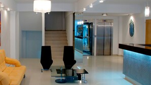 A modern lobby with a yellow sofa, a glass coffee table, a large abstract painting, a chandelier, and a reception desk. - Lofts & Suites Rosario (Rosario)
