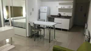 A compact hotel room with a bed, a kitchenette, a dining area with a table and chairs, and a green sofa. - Lofts & Suites Rosario (Rosario)
