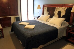 Una cama bien hecha con una colcha oscura estampada, dos almohadas y una toalla doblada sobre la cama.