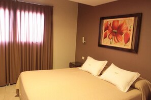 Una habitación de hotel con cama, cortinas, un cuadro y una mesita de noche.