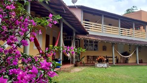 A two-story building with a covered patio area, a hammock, and a sign reading "RECEPTION". - Hotel Pousada Caminho da Praia (Guarapari)