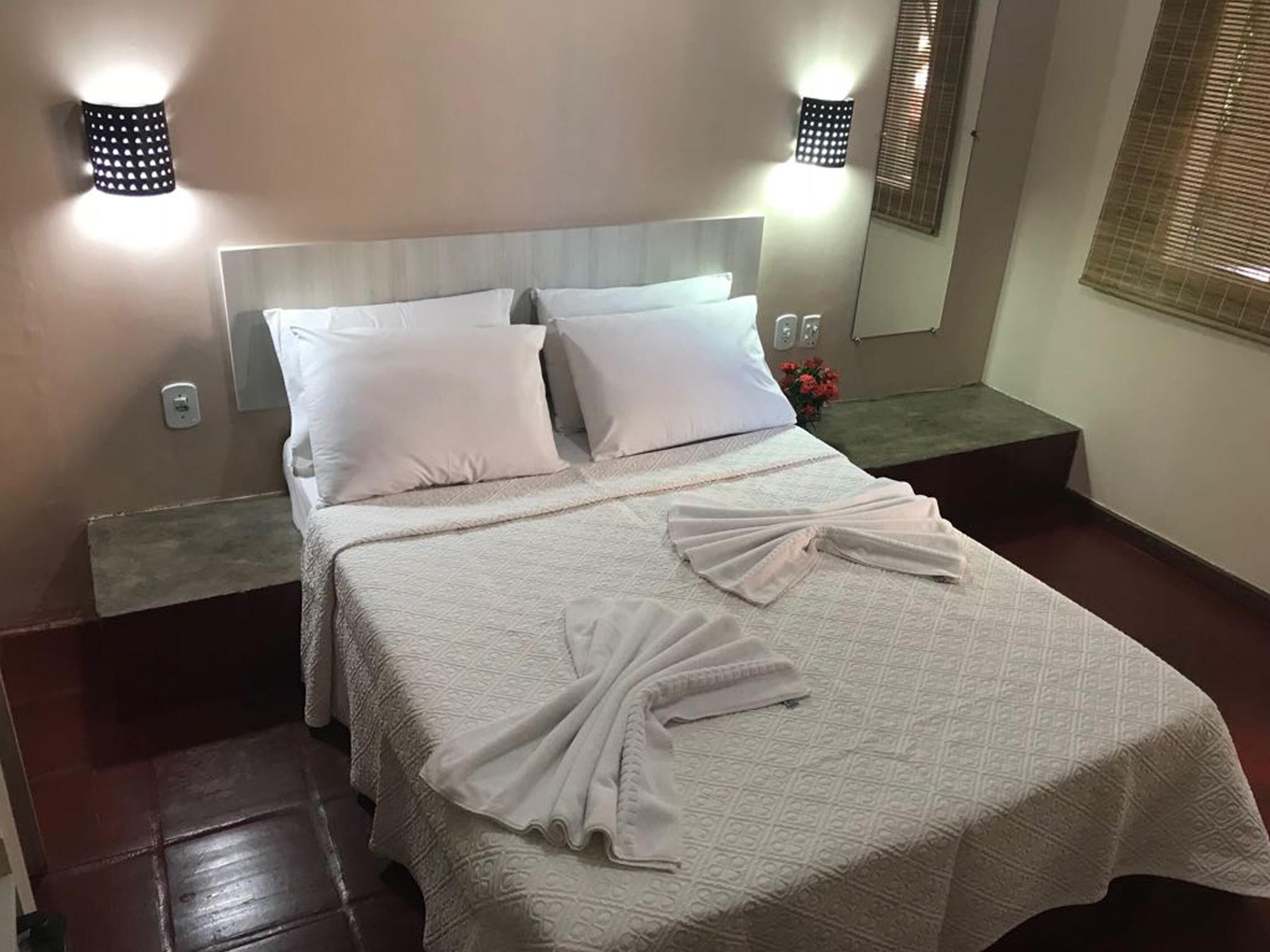 A neatly made bed with white linens, a headboard, and two wall-mounted light fixtures.