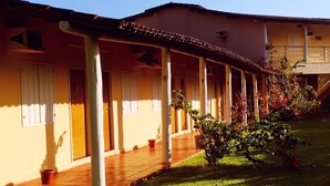 A building with a covered walkway, columns, and a garden area. - Hotel Pousada Caminho da Praia (Guarapari)