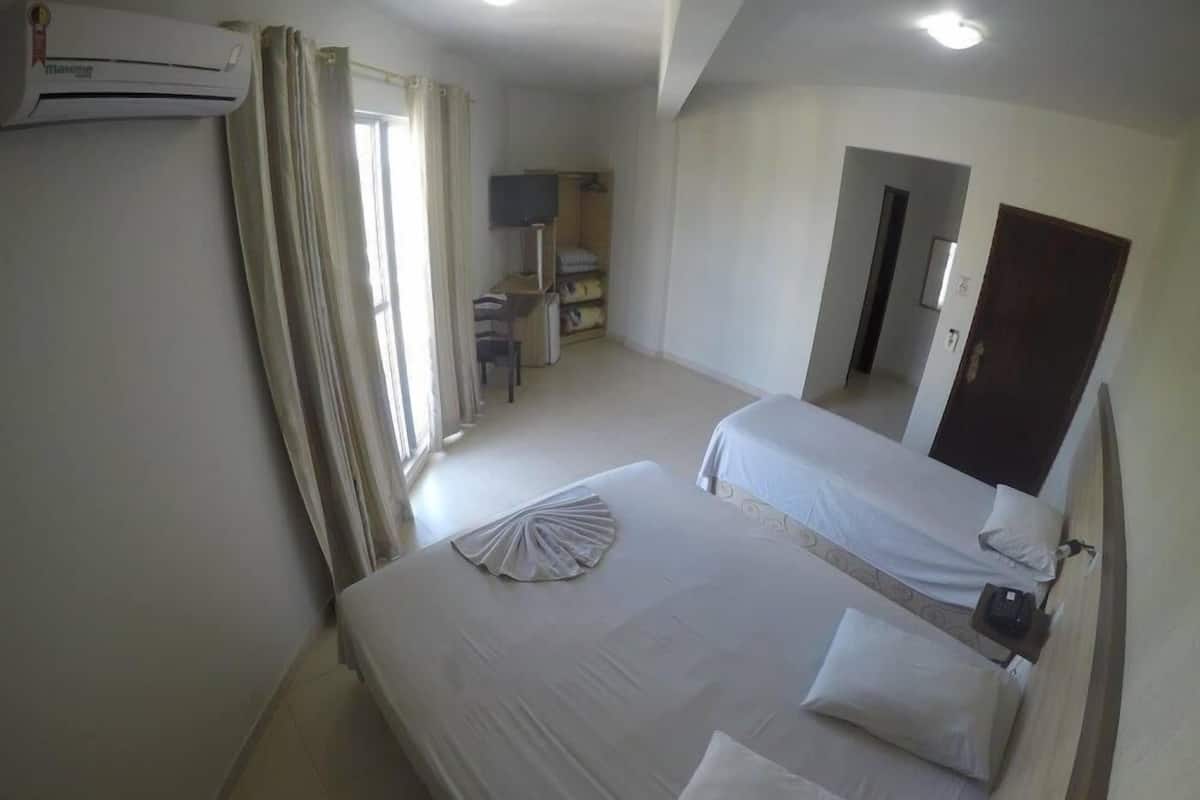 A hotel room with two beds, a desk, a chair, a TV, and an air conditioning unit.