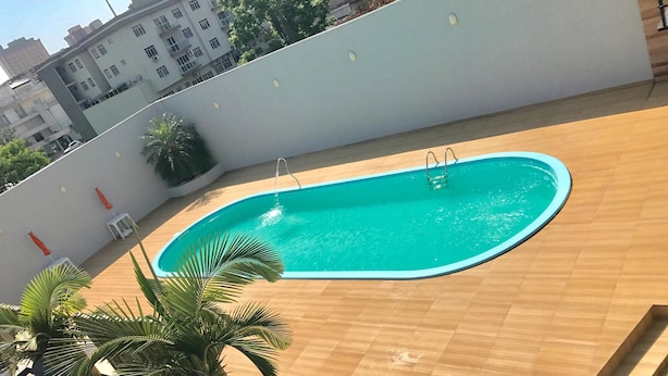 Una piscina amb un pont de fusta, envoltada per una paret baixa i palmeres.