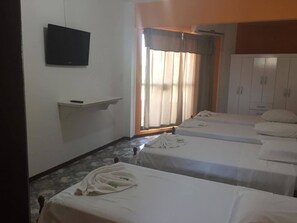 A hotel room with two single beds, a TV mounted on the wall, a small shelf, and a window with curtains. - Hotel Skala (Foz do Iguaçu)