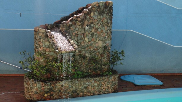 A stone water feature with a cascading waterfall next to a swimming pool. - Hotel Skala (Foz do Iguaçu)