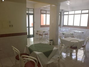 A dining area with white tables and chairs, a green table runner, and a tiled floor. - Hotel Skala (Foz do Iguaçu)