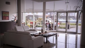 A modern living room with a white sofa, a coffee table, and large windows offering a view of an outdoor patio area. - Alto Miramar Resort & Spa (Miramar)