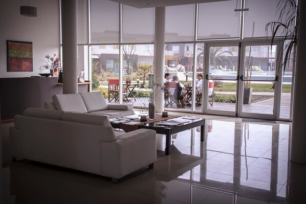 Una sala de estar moderna con un sofá blanco, una mesa de centro y grandes ventanas que ofrecen vistas a un patio exterior.