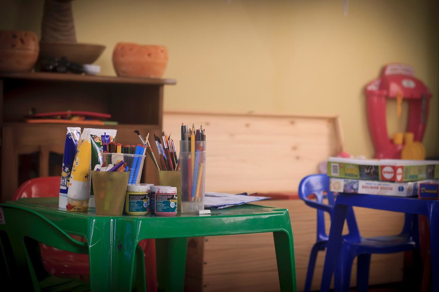 A room with a green table holding art supplies, a blue chair, and a shelf with pottery.