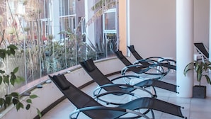 A waiting area with reclining chairs, large windows, and a view of a building with balconies. - Alto Miramar Resort & Spa (Miramar)