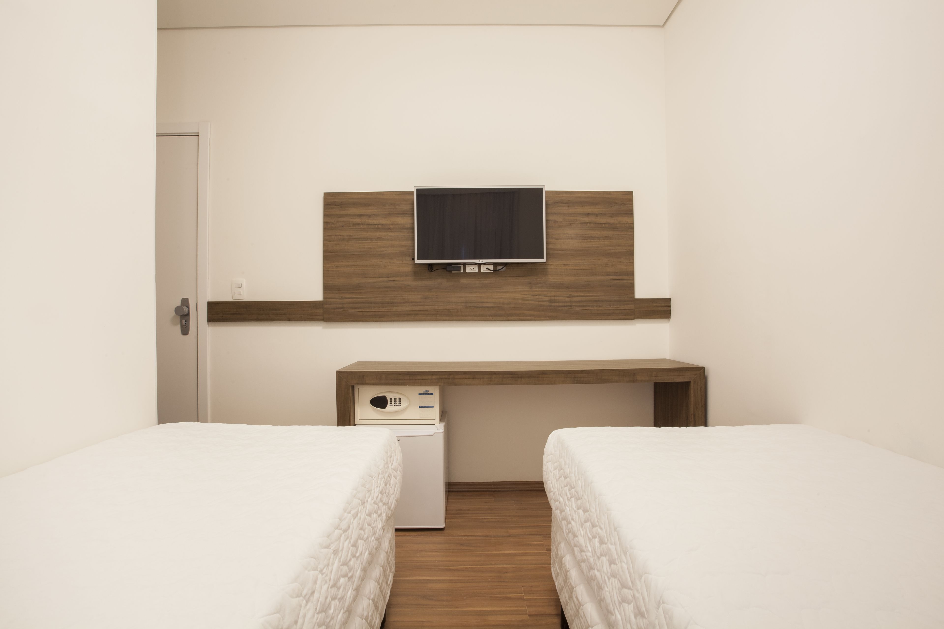 A hotel room with two beds, a TV mounted on the wall, a small desk, and a washing machine.