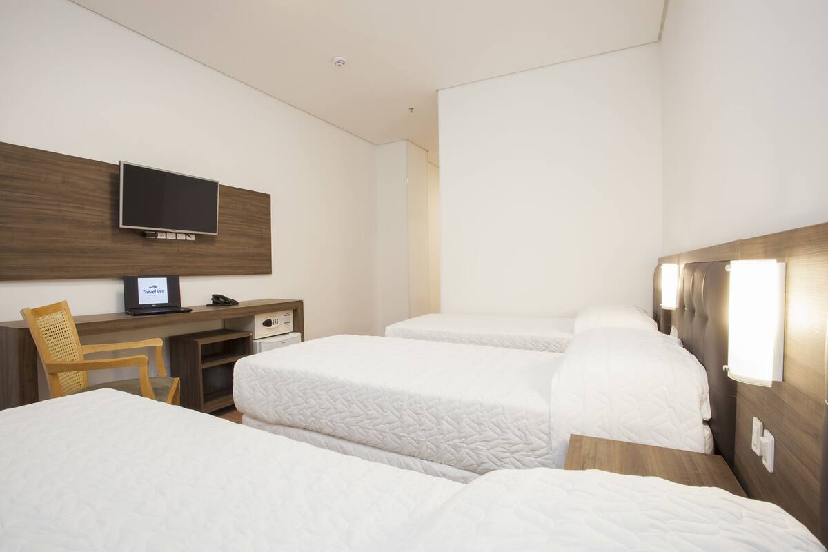 A hotel room with two beds, a desk with a TV, a chair, and a wooden headboard.
