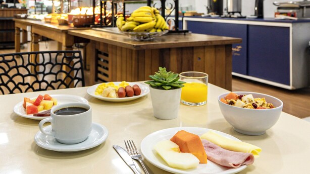 A breakfast setting with plates of food, a cup of coffee, a glass of orange juice, and a bowl of cereal. - Travel Inn Express Hotels Brás (São Paulo)