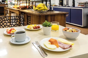 Una colazione servita con piatti di cibo, una tazza di caffè, un bicchiere di succo d'arancia e una ciotola di cereali.