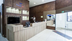 A Travel Inn reception desk with a flat-screen TV, computers, and a digital display. - Travel Inn Express Hotels Brás (São Paulo)