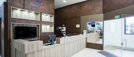 A Travel Inn reception desk with a flat-screen TV, computers, and a digital display.