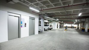A multi-level parking garage with concrete floors and white walls, featuring several parked cars and visible structural columns. - Travel Inn Express Hotels Brás (São Paulo)