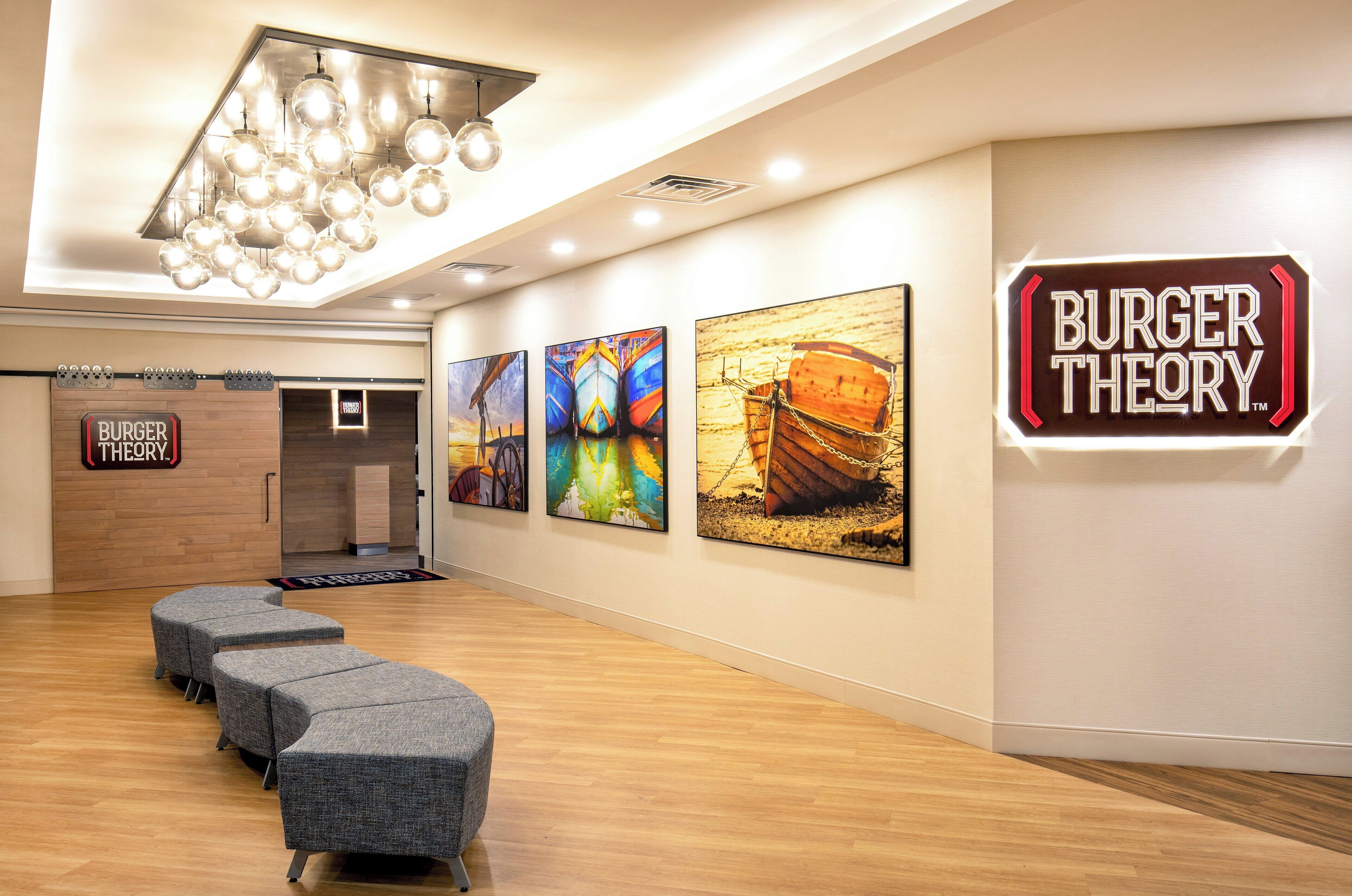 A modern interior with a reception area, a Burger Theory sign, and a row of grey upholstered seating.