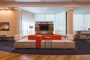 Una habitación de hotel moderna con un sofá grande, un televisor de pantalla plana y una pequeña mesa.