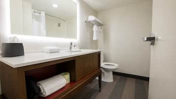 Un baño con lavamanos blanco, espejo, inodoro, tocador de madera y un perchero para toallas.