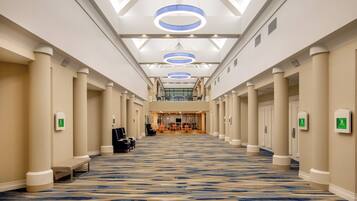 A hotel corridor with a patterned carpet, columns, and a seating area with chairs.