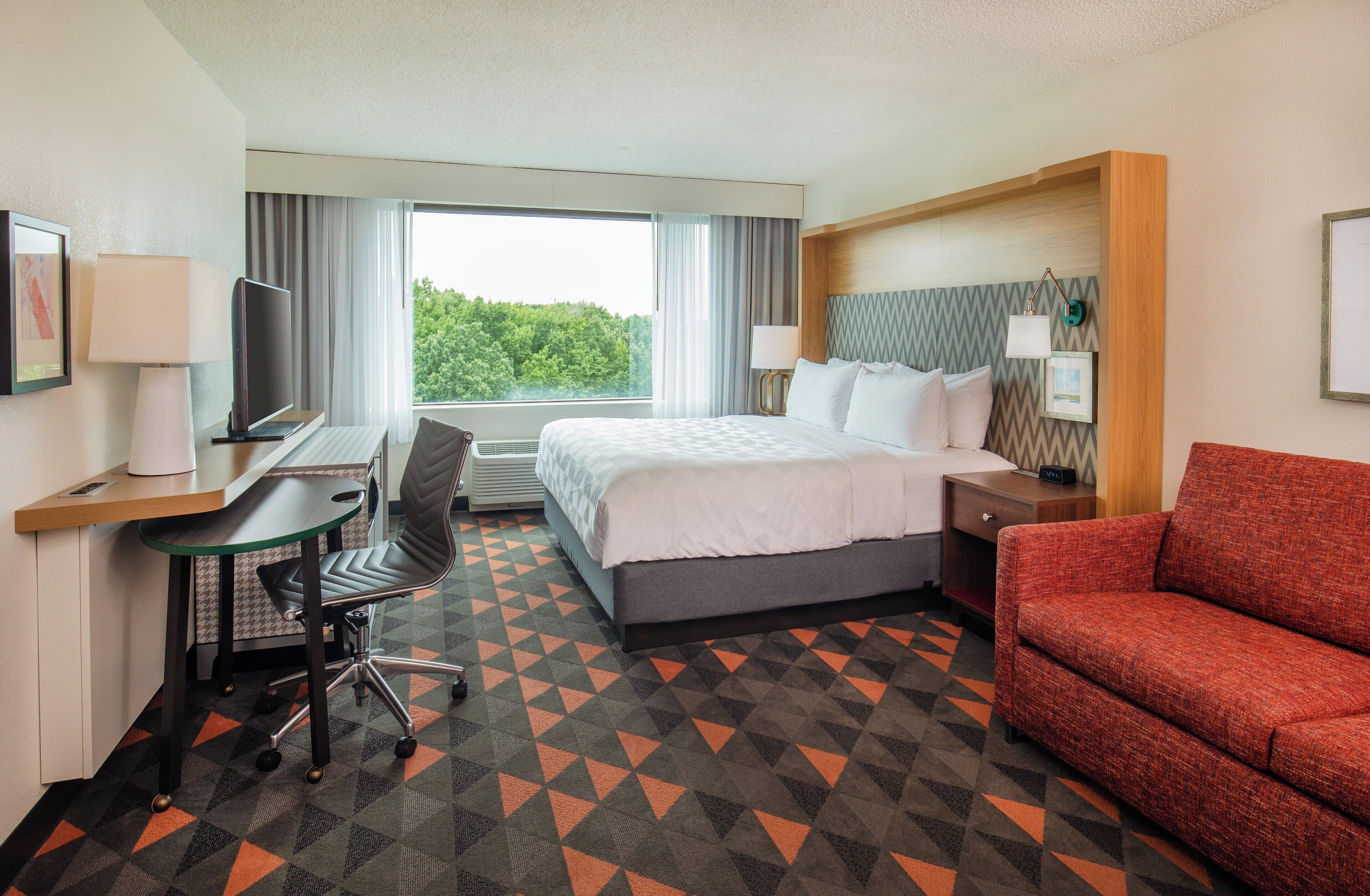 A hotel room with a bed, desk, chair, and a red sofa.