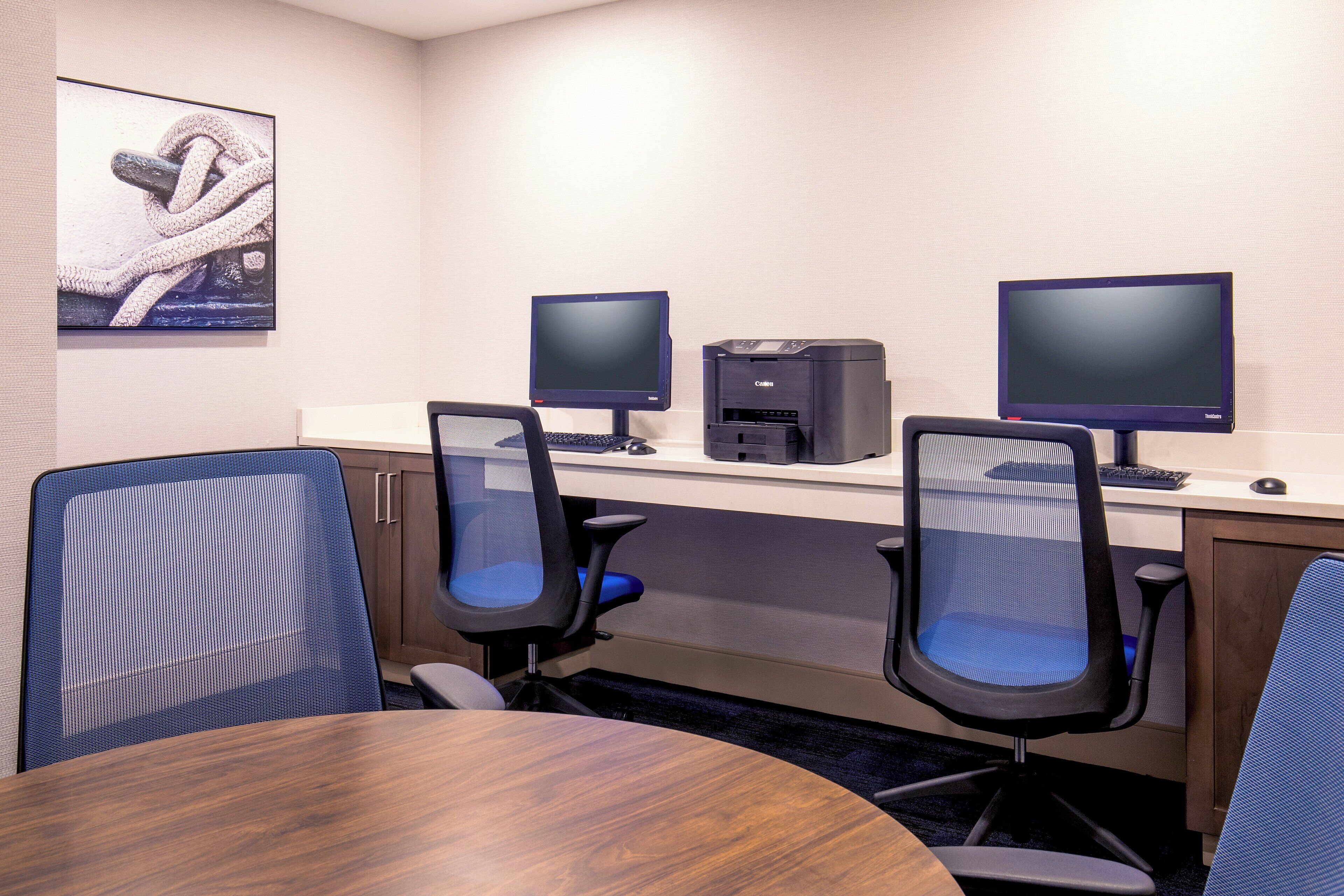 A conference room with a round table, four office chairs, two monitors, a printer, and a poster on the wall.