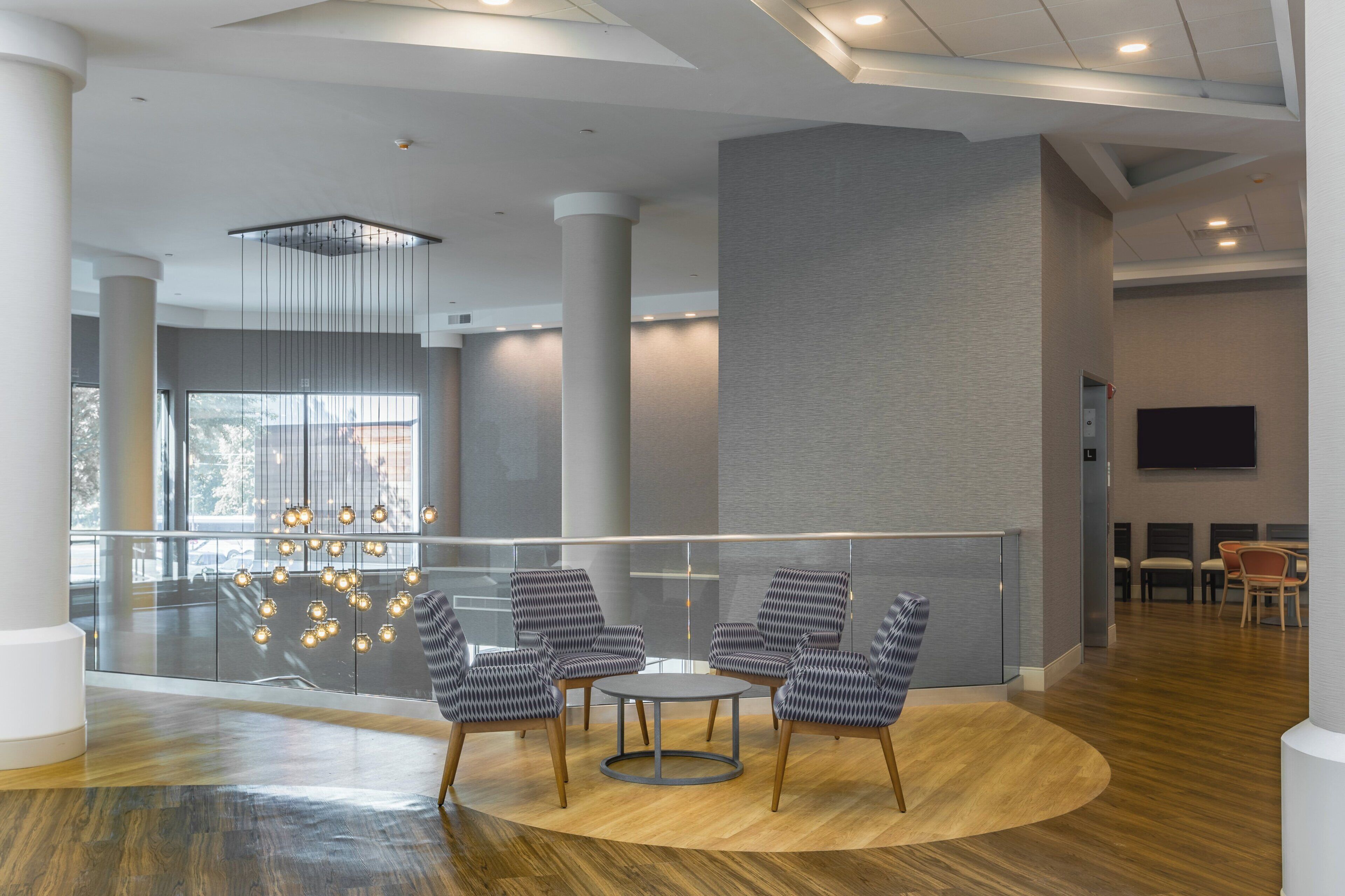 A modern lobby with a glass railing, a round table with chairs, and a large pillar.