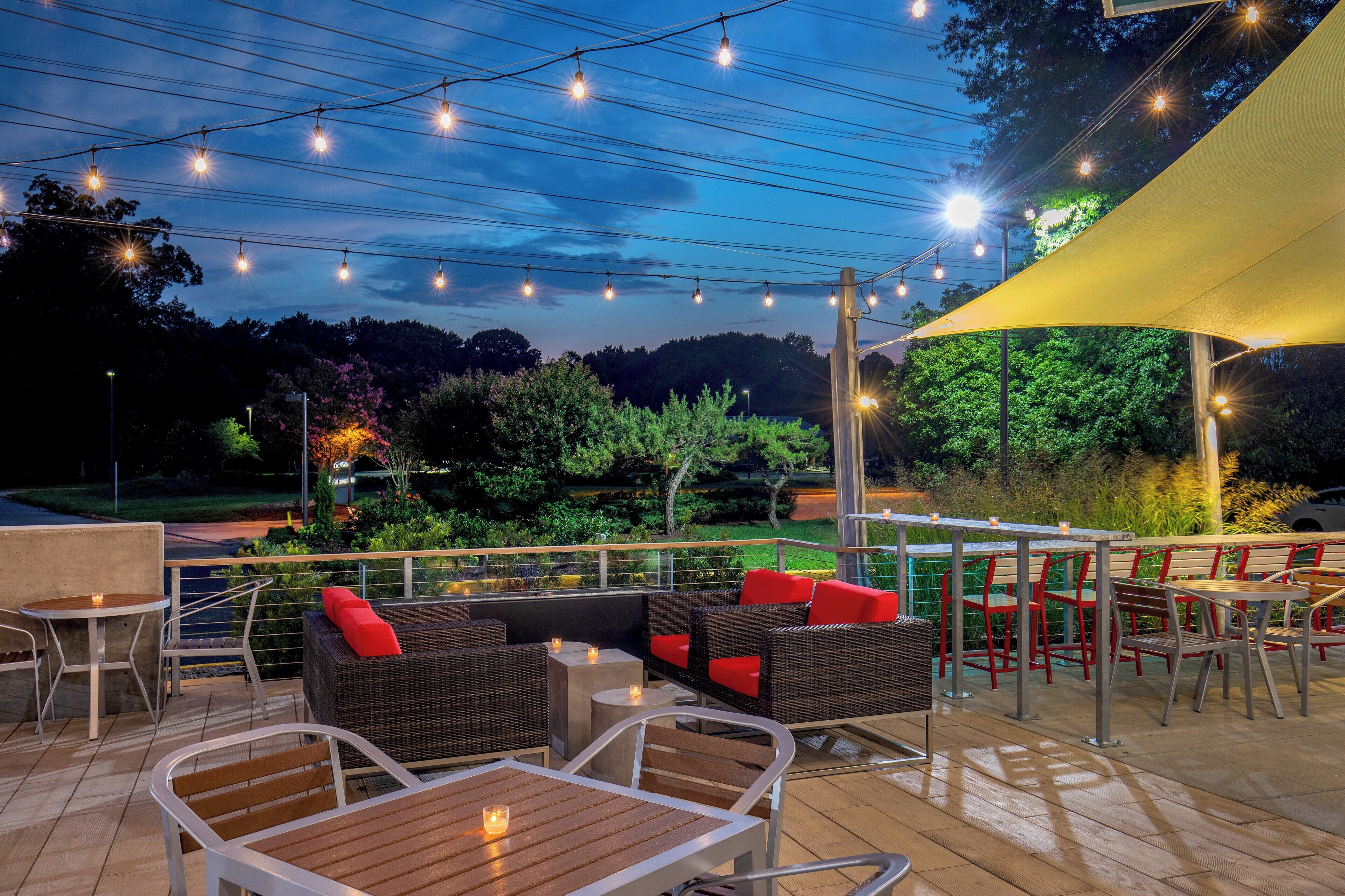 An outdoor seating area with tables and chairs, a yellow canopy, and string lights against a twilight sky.
