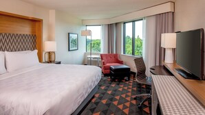 Une chambre d’hôtel avec un grand lit, un bureau avec une télévision, une chaise, une petite table et une fenêtre donnant sur un beau paysage.