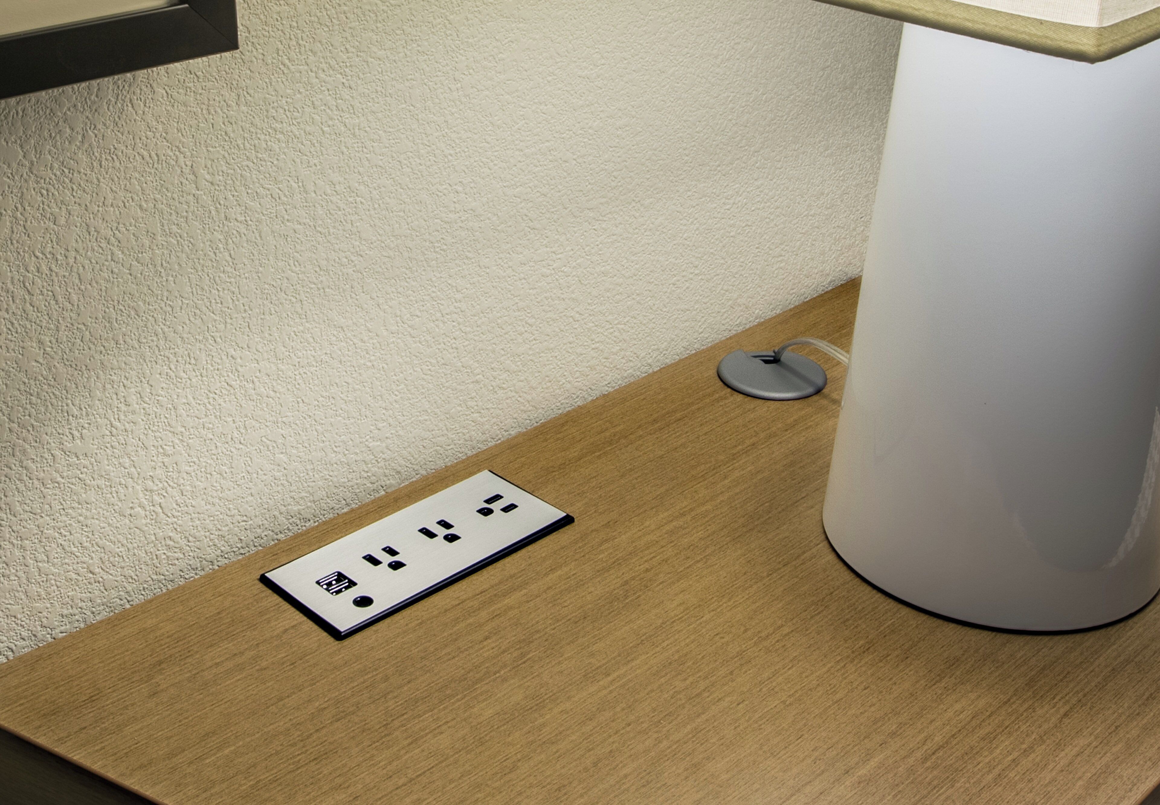 A power outlet on a wooden surface next to a white lamp.
