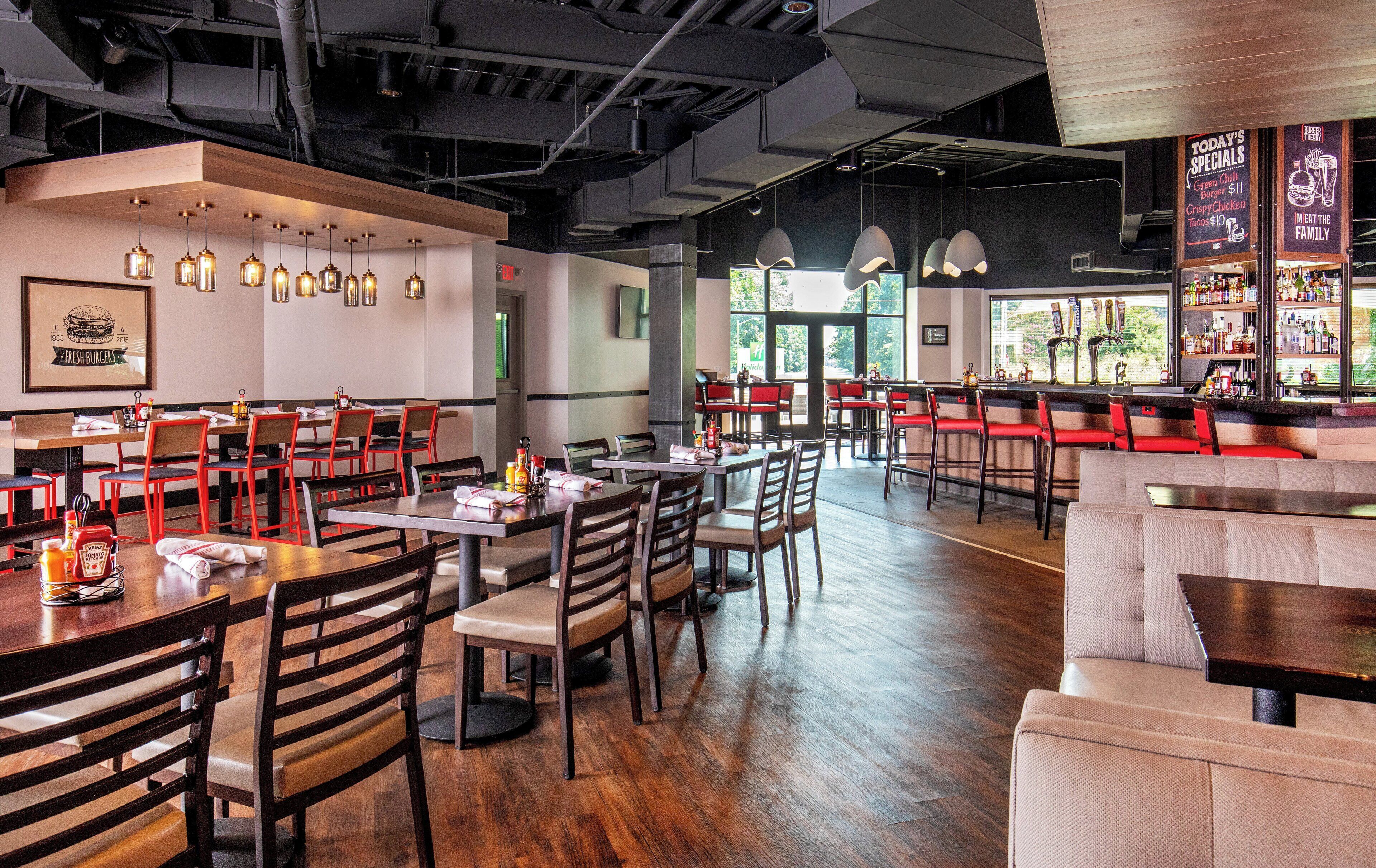 A restaurant interior with multiple dining tables and chairs, a bar area, and a menu board displaying specials.