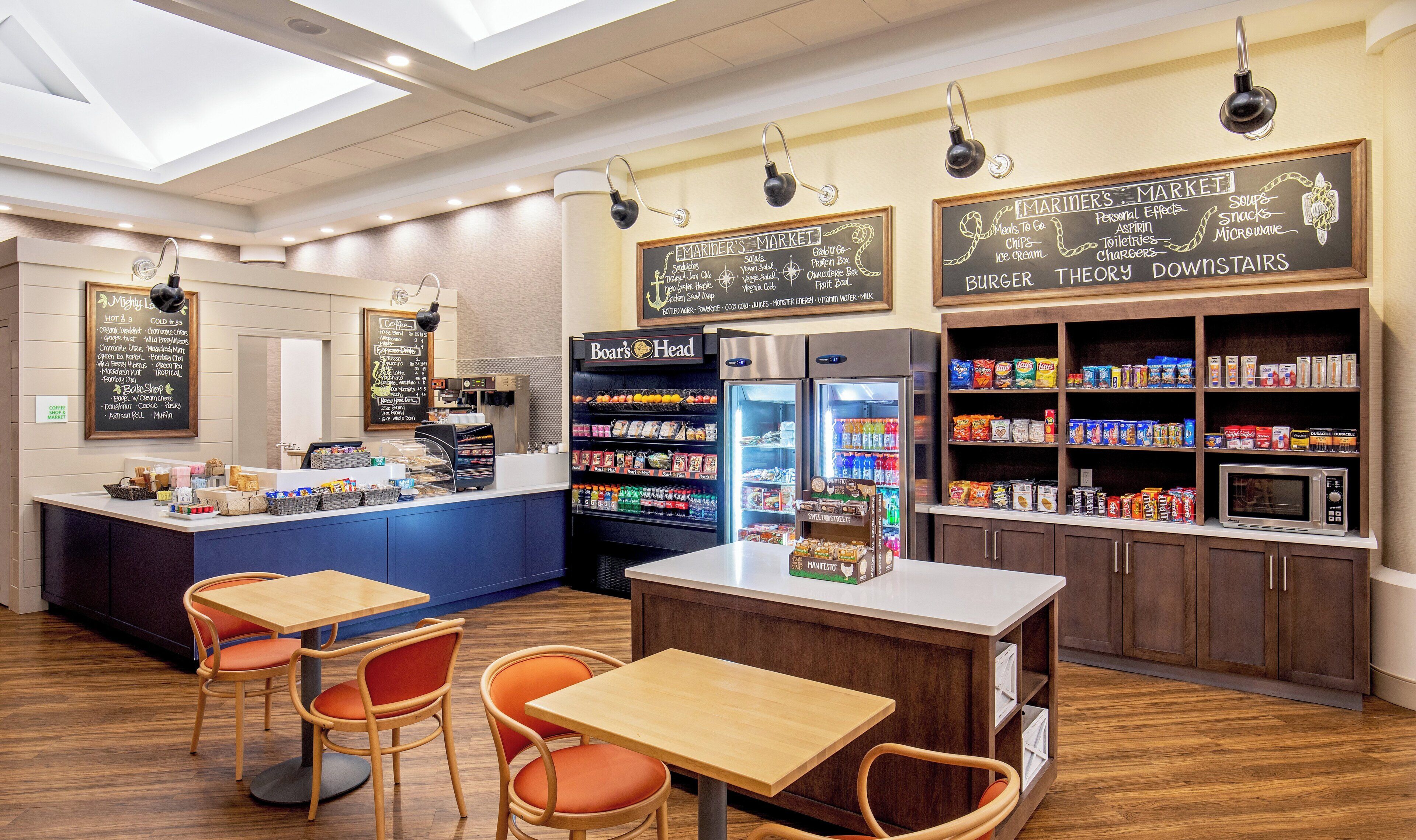 Una cafetería con barra de café, zona de estar y nevera llena de bebidas.