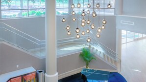Un intérieur moderne avec un escalier, une table en verre et des lampes sphériques suspendues.