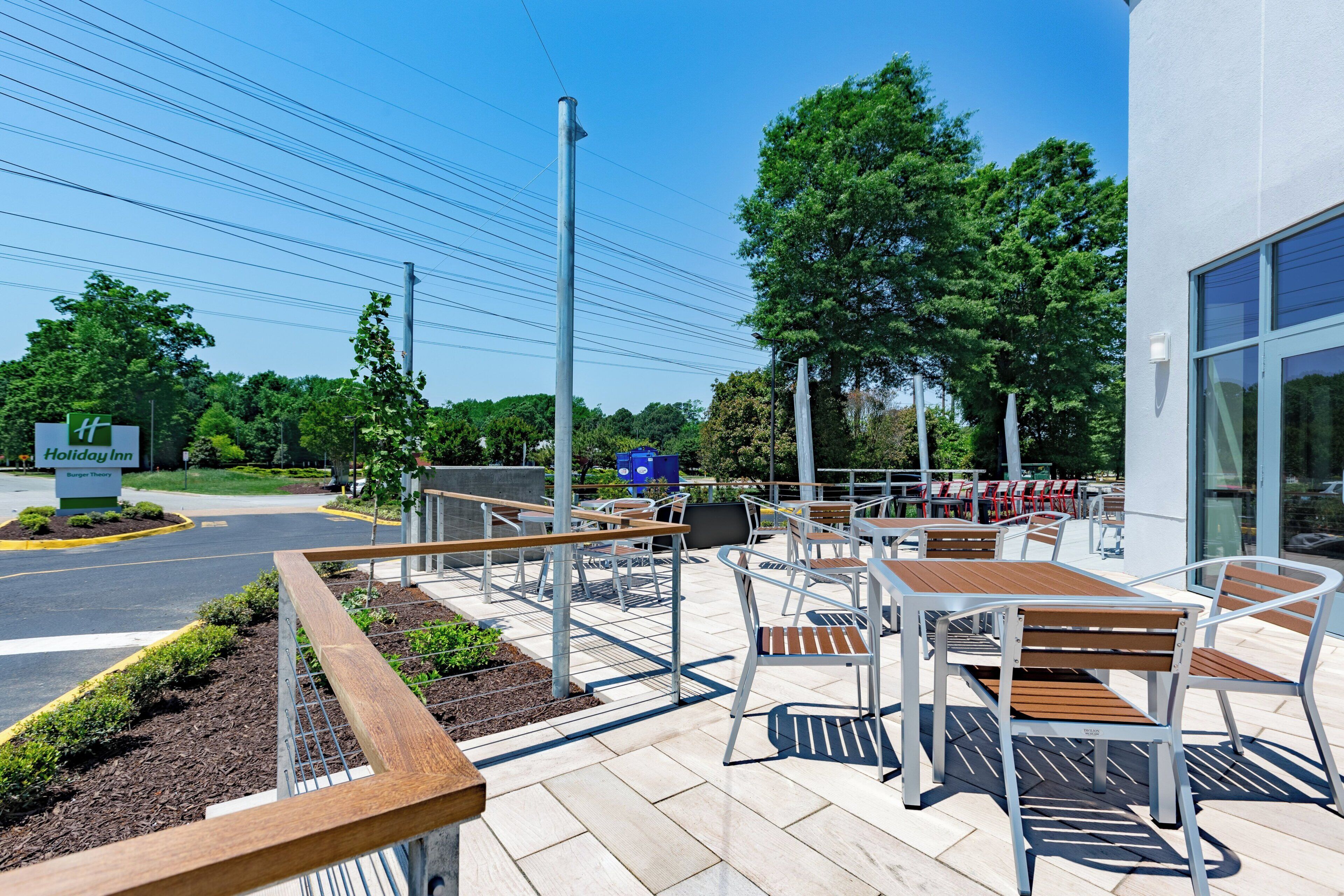 An outdoor patio with tables and chairs, a Holiday Inn sign, and a building with large windows.