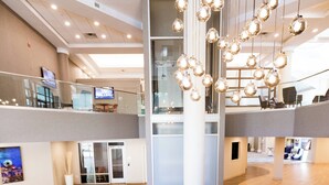 Un hall d’entrée moderne avec un grand piano, un plafond haut et un lustre contemporain.