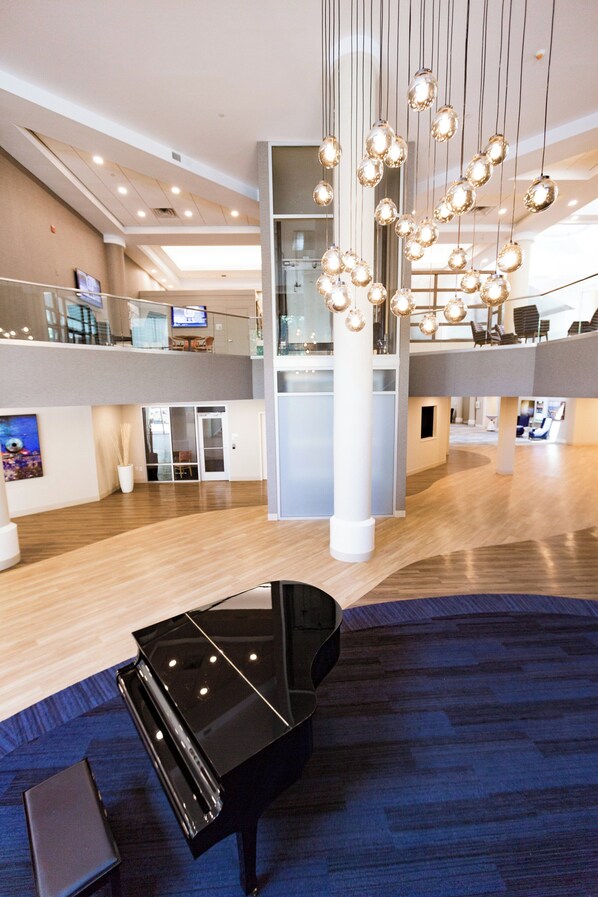 Een moderne lobby met een vleugelpiano, een hoge plafond en een moderne kroonluchter.