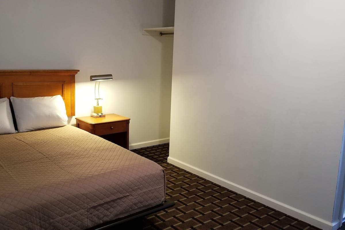 A hotel room with a bed, two pillows, a nightstand with a lamp, and a brick-patterned floor.