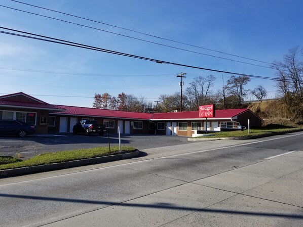 A Budget Inn with a red roof and a signboard. There are two cars parked in front, and a grassy area with a sidewalk. - Budget Inn Breezewood (Breezewood)