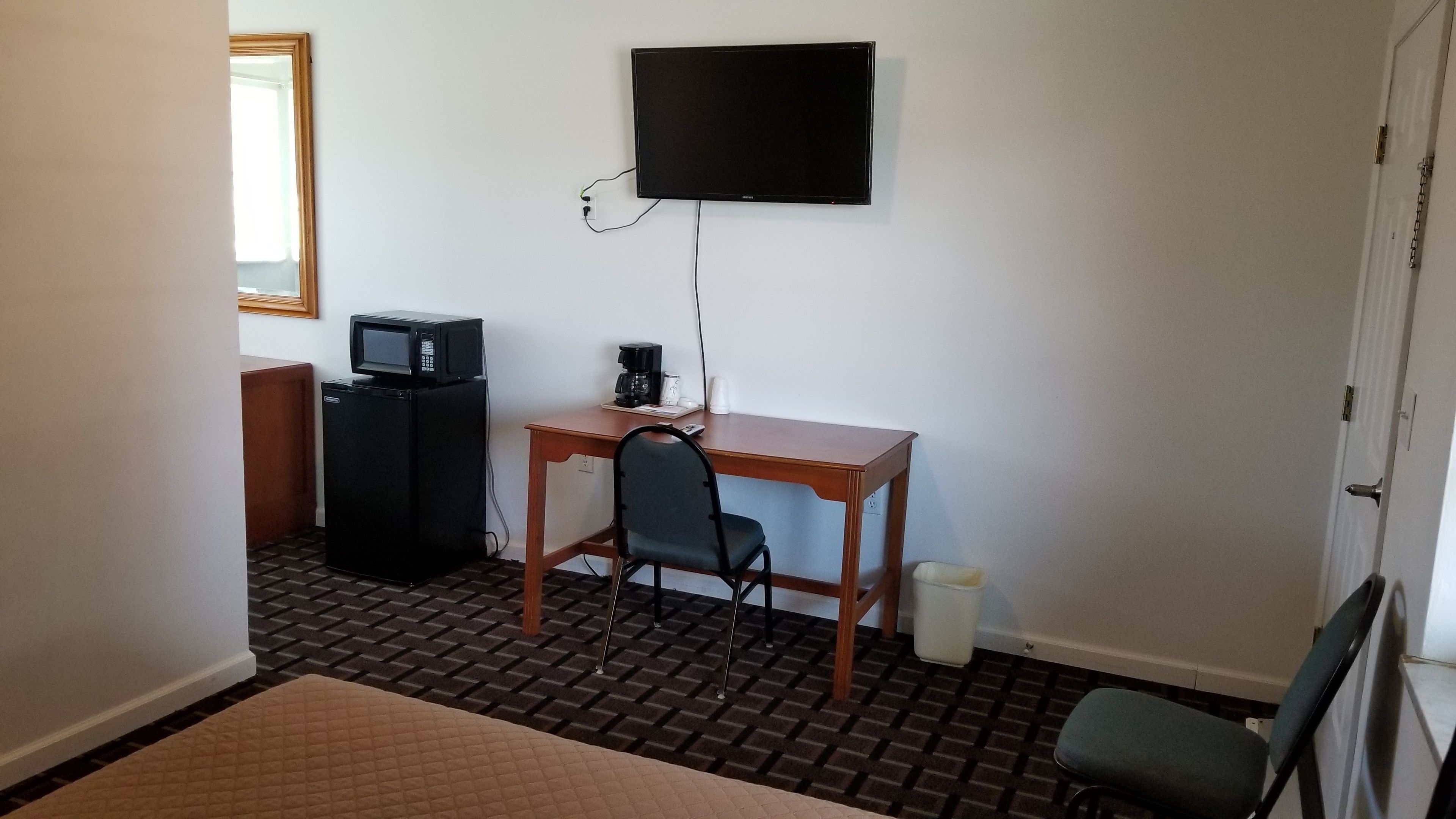A compact hotel room with a kitchenette, a desk, a chair, and a television mounted on the wall.