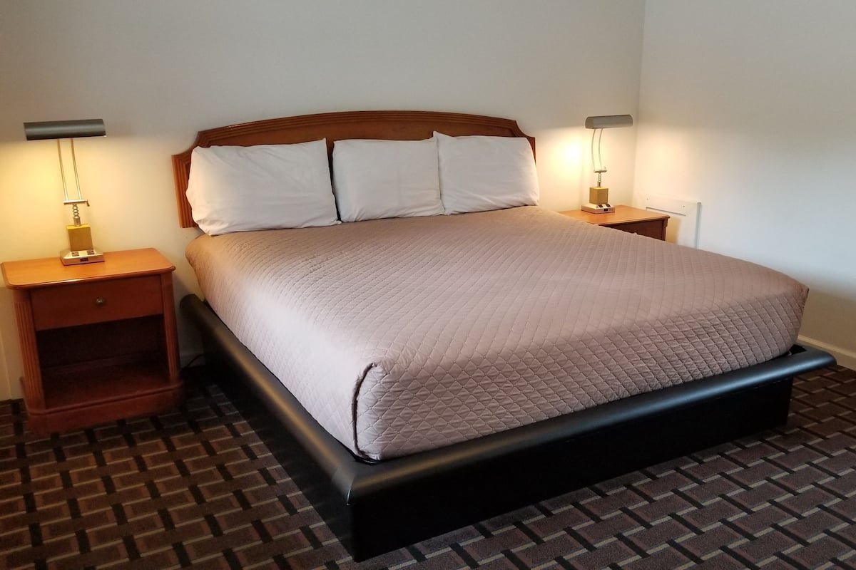 A neatly made bed with a wooden headboard, two bedside tables with lamps, and a patterned floor.