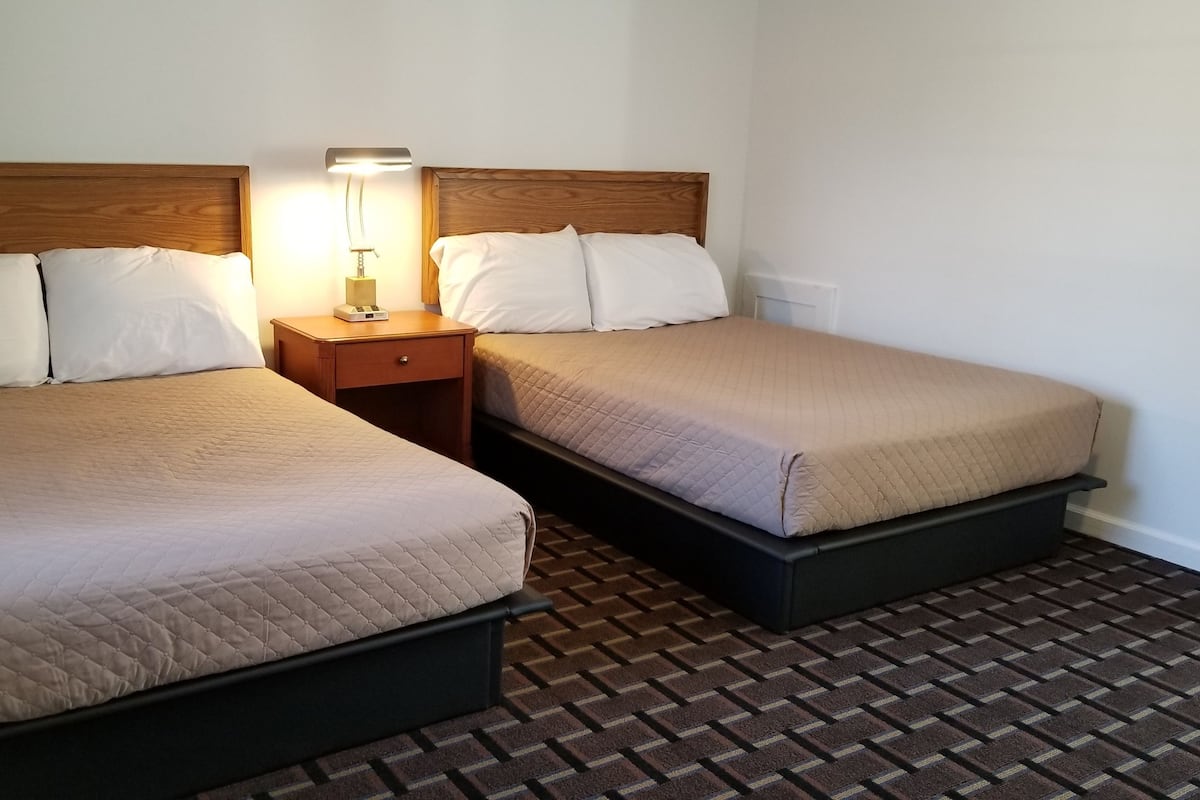 A hotel room with two beds, a nightstand with a lamp, and a patterned floor.