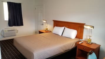 A hotel room with a bed, two bedside tables with lamps, a heater, a window with curtains, and a door.