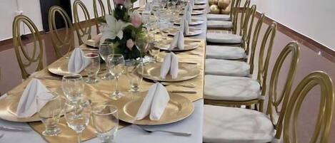 A long banquet table set with gold and white tableware, surrounded by gold chairs.