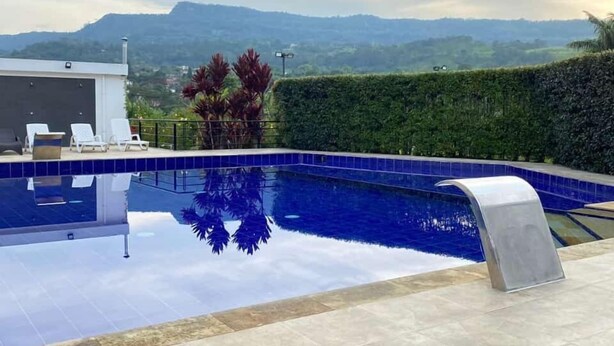 Une piscine avec vue sur les montagnes, un espace abrité avec des chaises longues et une haie bien entretenue.